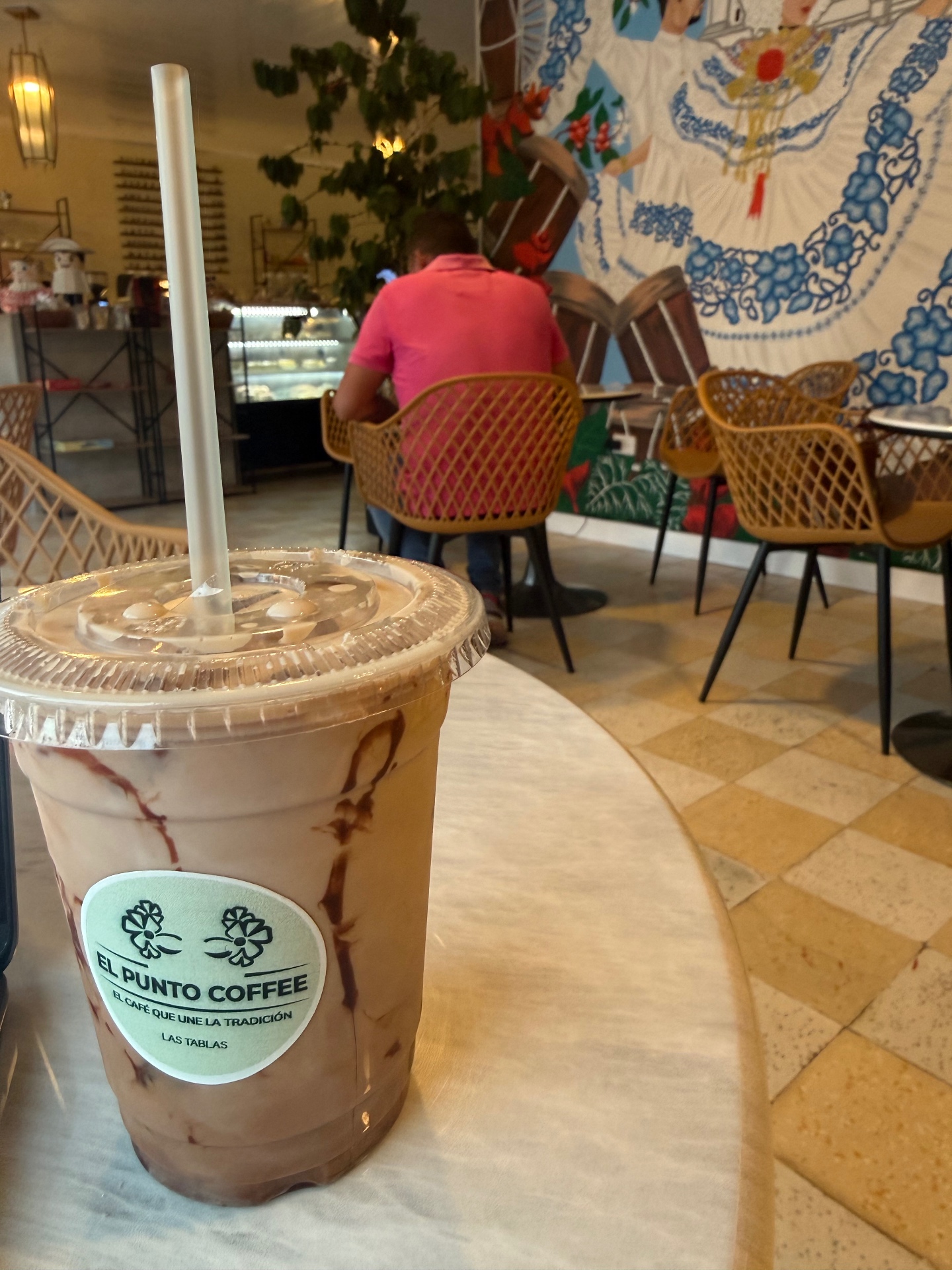 Iced mocha de El Punto Coffee con interior y mural de pollera al fondo